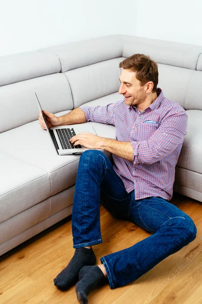 Uomo con computer portatile seduto sul pavimento — Foto Stock