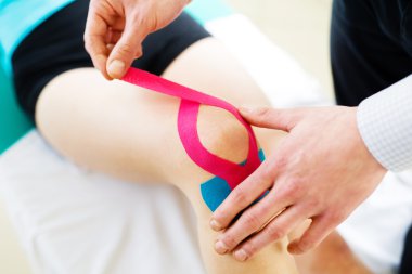 Therapist applying tape to patient knee clipart
