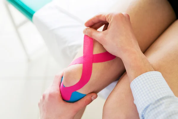 Therapist applying tape to patient knee — Stock Photo, Image