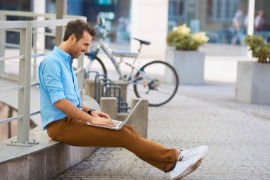 Genç adam dizüstü bilgisayarla oturuyor.