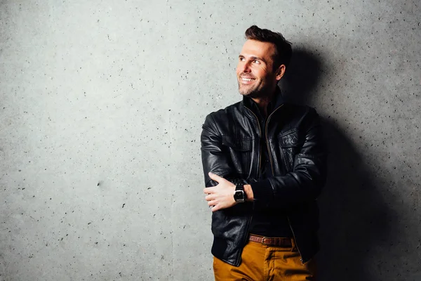 Homem feliz em jaqueta de couro em pé junto à parede — Fotografia de Stock