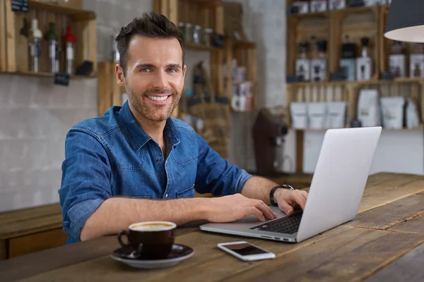 Hombre guapo sentado en la cafetería con portátil — Foto de Stock