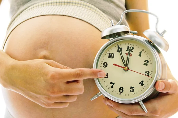 Молодая беременная женщина с будильником — стоковое фото