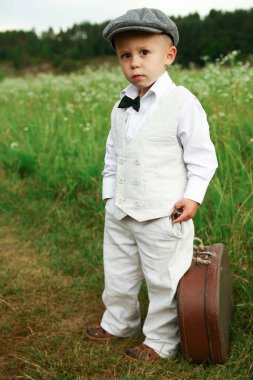 Şapkalı çocuk, yol kenarında bavulu var.