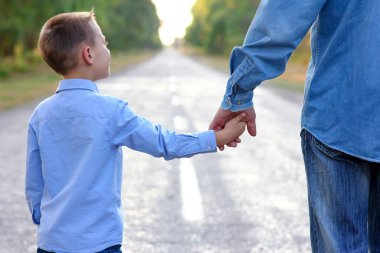 Anne ve baba mutlu bir çocuğun elini tutup yolda yürüyorlar.