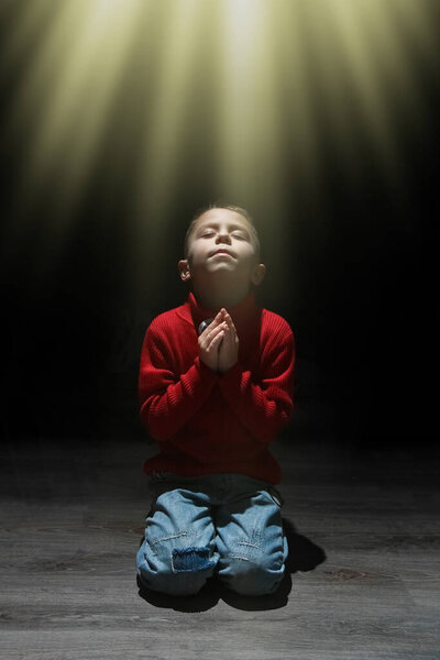 Child praying spiritually to God on a black background