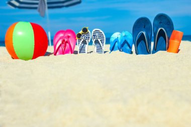 Plaj yaz tatili afişi. Parmak arası terlik ve şapkalı, üzerinde tahta ve top olan okyanus kıyısındaki kumda. Deniz kıyısında yaz aksesuarları. Tropik tatil ve rahat seyahat konsepti. Üst görünüm ve kopyalama alanı.