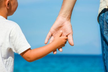Mutlu baba, Yunan Denizi kıyısında bir çocuğun elini tutuyor.