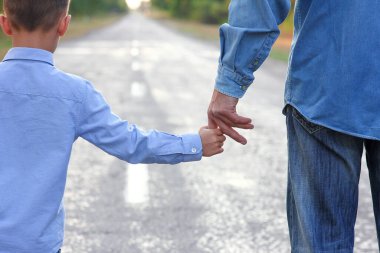 Ebeveyn küçük bir çocuğun elini tutar ve yolda yürür.