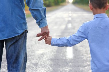 Ebeveyn küçük bir çocuğun elini tutar ve yolda yürür.