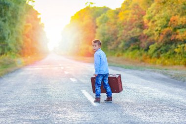 Parka giderken yolda bavulu olan mutlu çocuk.
