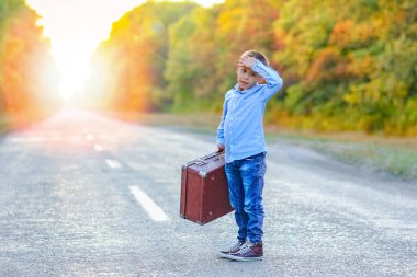 Parka giderken yolda bavulu olan mutlu çocuk.