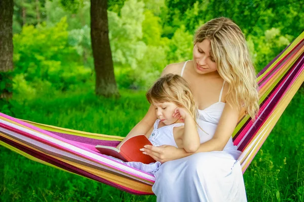 快乐的母亲带着一个孩子在自然公园的吊床上看书 — 图库照片