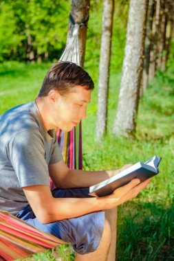 Hamakta mutlu bir adam parkta doğa üzerine bir kitap okuyor.