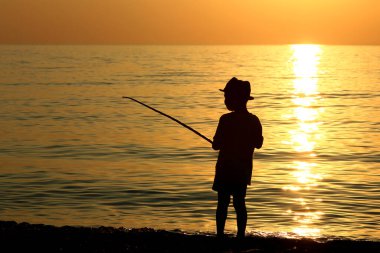Denizde oltayla gezen bir çocuğun silueti.