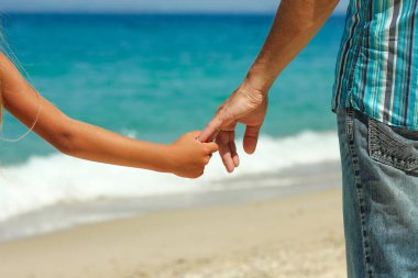 Ebeveyn yazın plajda çocuğun elini tutar.