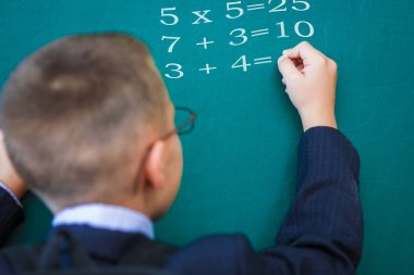 Okul çantasıyla tahtada duran ve gözlük takan mutlu çocuk.