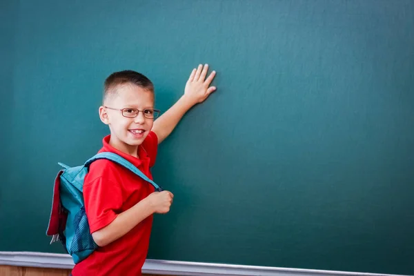 快乐的孩子站在黑板前 背着上学用的背包 戴着眼镜 — 图库照片