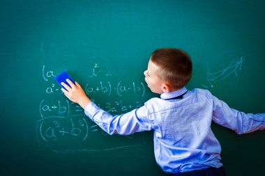 Derste okul tahtasının başında duran mutlu çocuk.