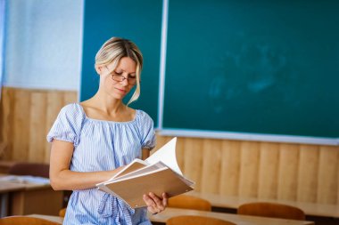 Sınıfta kitapları olan mutlu bir öğretmen okula geri döndü.