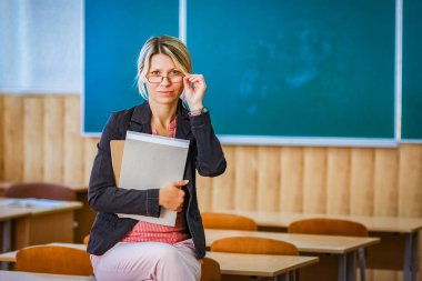 Sınıfta kitapları olan mutlu bir öğretmen okula geri döndü.