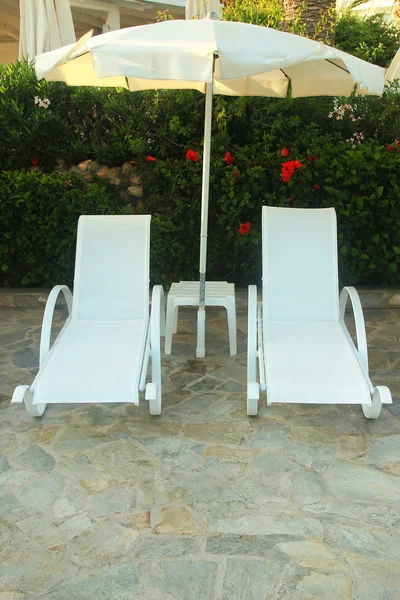 Camas de sol e guarda-chuva à beira da piscina — Fotografia de Stock