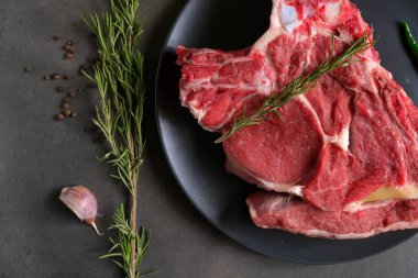 Esmer arka planda çeşitli otlar ve baharatlarla çiğ biftek. Yukarıdan görüntüle.