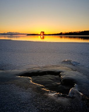 Sahilde gün batımı ve ön planda kar.