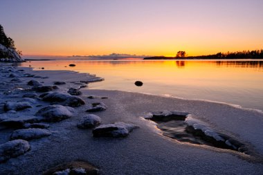 Sahilde gün batımı ve ön planda kar.
