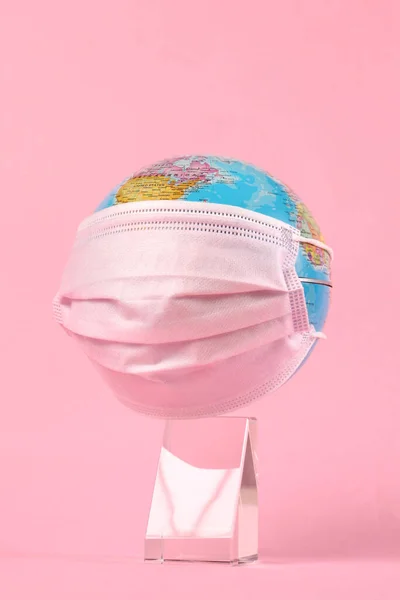 medical face mask cover a globe on pink background with copy space for your text