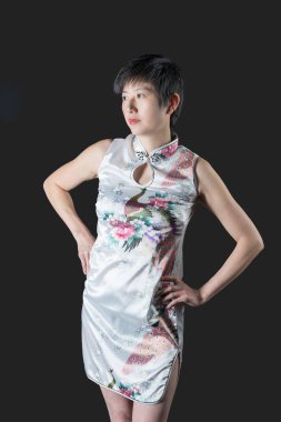 Kısa beyaz çiçek desenli, kısa geleneksel elbisesi olan Çinli kadın elleri kalçasında sağına bakıyor.