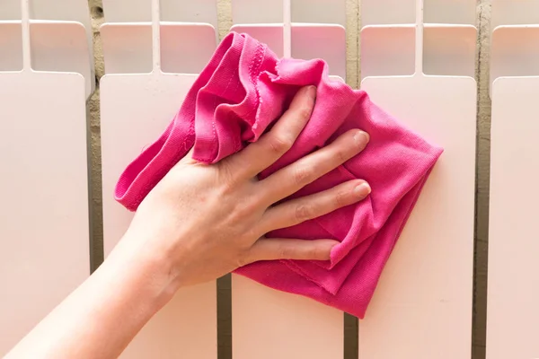 Bir kadın radyatörü tozdan ve pislikten bez parçasıyla temizliyor..