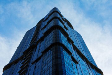 Bulutlu gökyüzünün arka planına karşı camdan yapılmış çok katlı modern bir bina..