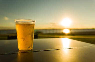 Guaiba rıhtımında gün batımında masada plastik bardak soğuk bira.