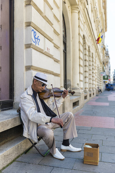 Бедняга в белом костюме и галстуке играет на скрипке, чтобы заработать немного
 