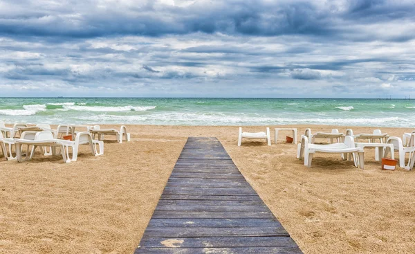 Playa de arena en día nublado con camino de madera y tumbonas vacías Fotos de stock libres de derechos