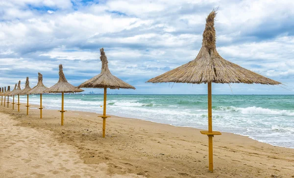 Beautifull empty beach in a windy day with straw umbrellas — Stock Photo, Image