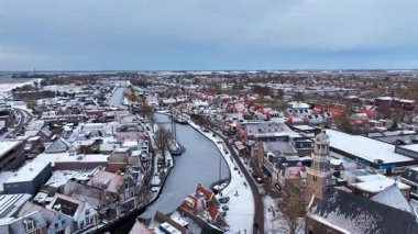 Soğuk koşullarda görünen binalar, sokaklar ve su yollarıyla karla kaplı bir şehri gösteren kış sahnesi..