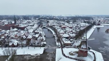 Geleneksel bir yel değirmeni ve çevresindeki binaların yer aldığı Avrupa 'nın tarihi bir kasabasının kış manzarası.