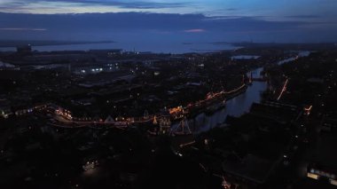 Geceleri limanda aydınlatılmış bir kilise ve geleneksel yelkenli gemilerinin yer aldığı tarihi bir Avrupa rıhtımı.