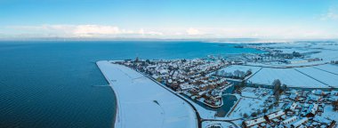 Kentsel mimarisi ve soğuk mevsimsel atmosferi olan büyük bir göl tarafından karla kaplı küçük bir Avrupa tarihi kasabasının havadan kış manzarası.