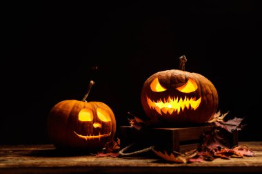 Parlak ya da parlak balkabağı lambası ve renkli, kuru sonbahar yaprakları. Kabaklı koyu bir arka plan, eski ahşap desenli bir masa. Korkunç Cadılar Bayramı konsepti