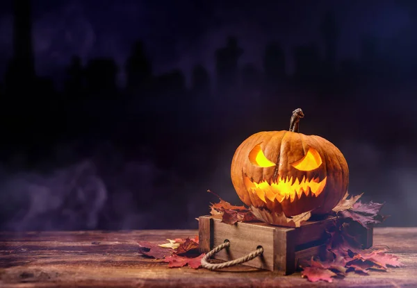 Halloween concept at night with pumpkin lamp. Still life of pumpkins and dry autumn leaves with smoke on the background. Old wood background.