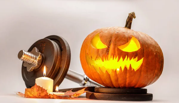 Scary Pumpkin head with candle. Dumbelle and pumpkin concept isolated on light gray background. Halloween concept, dry, colorful leaves.