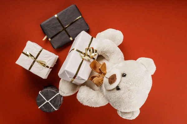Ours en peluche adorable blanc ou brun clair avec décorations et cadeaux de Noël. Concept de vacances avec peluche jouet ours et cadeaux de Noël sur la table rouge. — Photo