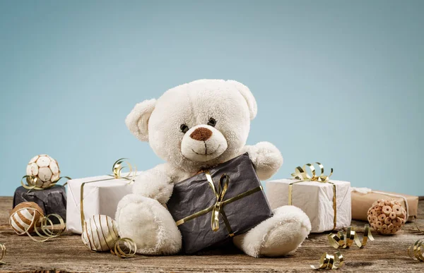 Beyaz ya da açık kahverengi sevimli, Noel süslemeleri ve hediyeleri olan oyuncak ayı. Oyuncak peluş ayıyla tatil konsepti ve ahşap masada noel hediyesi.. — Stok fotoğraf