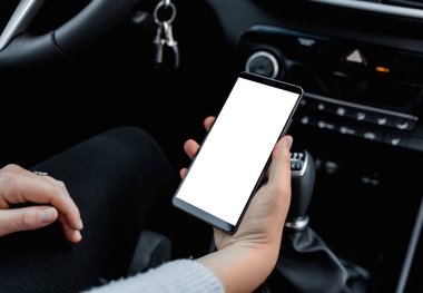 Genç bir kadının elinde izole edilmiş beyaz ekranlı cep telefonu modeli. Modern SUV arabasının iç mekanı. Arabasında akıllı telefon olan bir kadın model..
