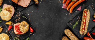 Lezzetli sosisli sandviçlerin düz kompozisyonu ve koyu arkaplanda farklı malzemeler vardı.