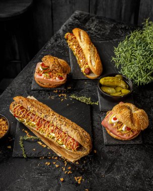 Farklı malzemelerle lezzetli sosisli sandviçler ve koyu arkaplanda kurutulmuş soğan.