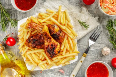 Bir porsiyon ızgara, kızarmış tavuk budu ve altın kahverengi kabuklu patates kızartması, rosmary, soğuk ve barbekü soslu beyaz bir tabakta servis ediliyor.